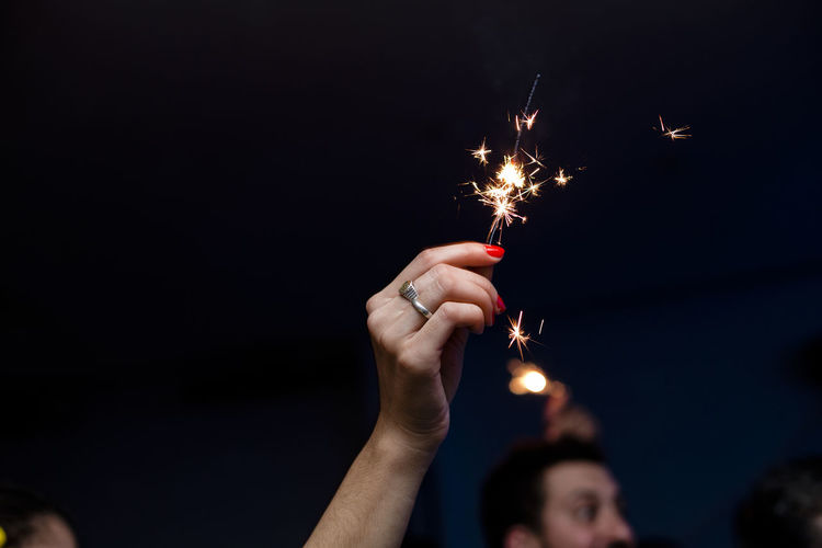 Cropped hand of woman holding lit sparkler at night