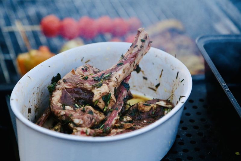 Close-up of herb-marinated lambmeat in a bowl in front of the smoky grill ready to cook it