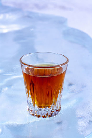 Glass of whiskey stands on white background of ice. orange drink in glass. top view from the side.