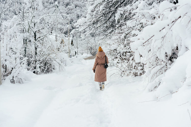 Back view of a woman in a coat and a yellow shake walking along a snowy path.