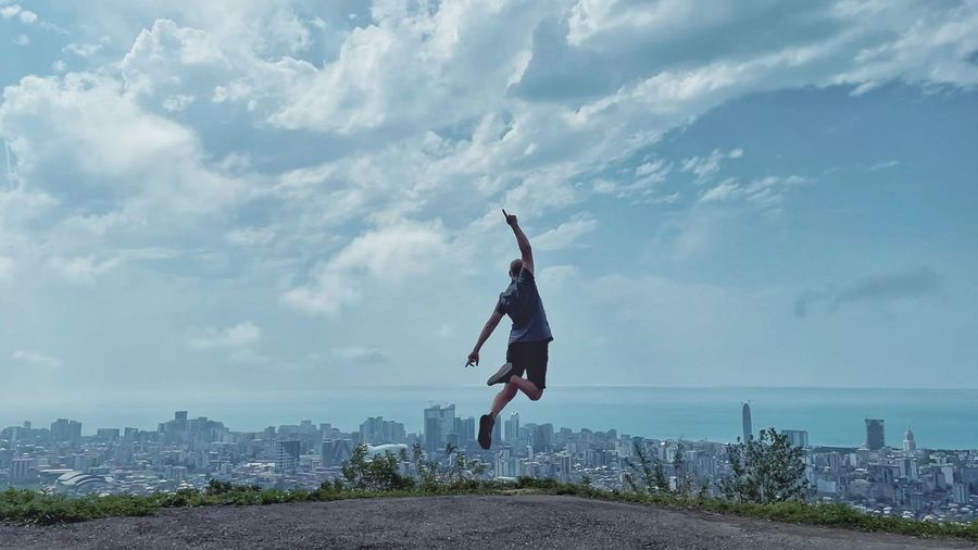 Side view of woman jumping over cityscape against sky