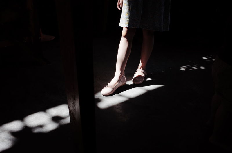 Low section of girl wearing shoes while standing on floor in darkroom