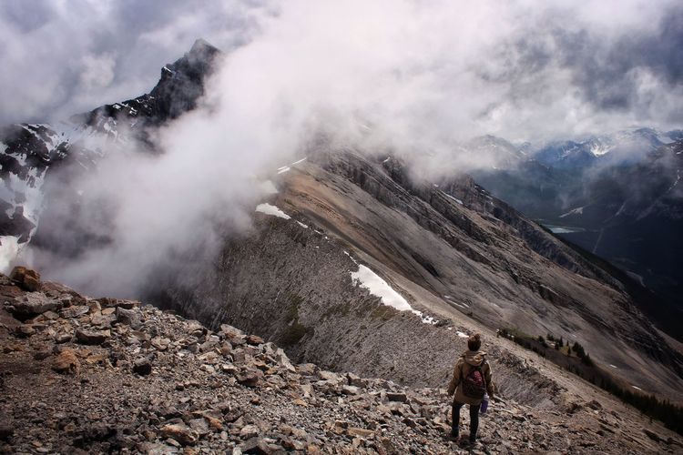Scenic view of hiker and cloud covered mountains against sky