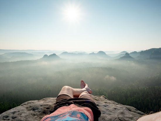 Hiker with bare feet lie on  edge of rock and relax. view over resting male body into morning land