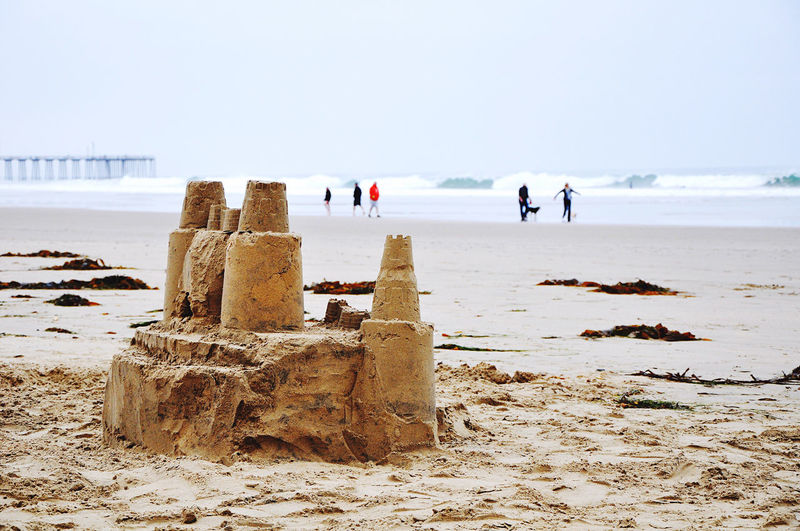 Sandcastle and people at beach against clear sky during winter