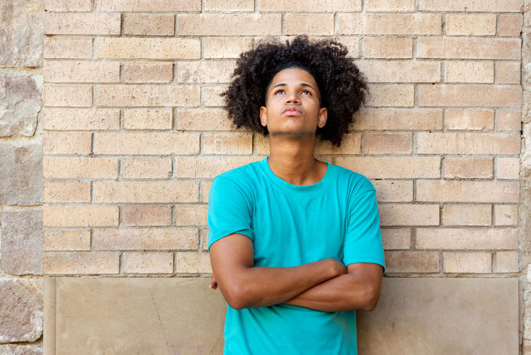 Portrait of serious young man standing against brick wall