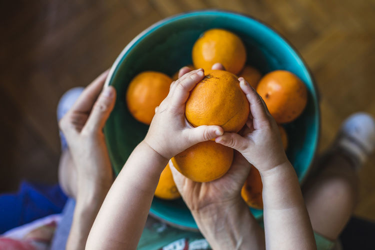 A mother and son place organic oranges in a green bowl.