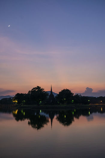 Silhouette temple and trees by lake against sky during sunset