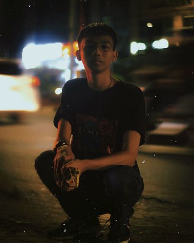 Portrait of young man crouching on road at night