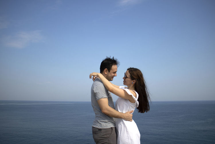 Young couple looking at each other standing in front of sea against sky