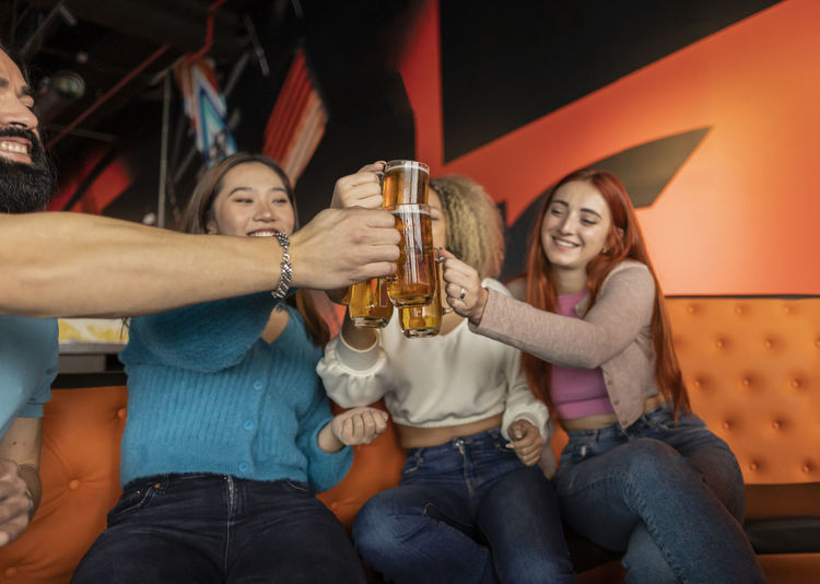 Happy multiracial friends toasting beer in bowling alley