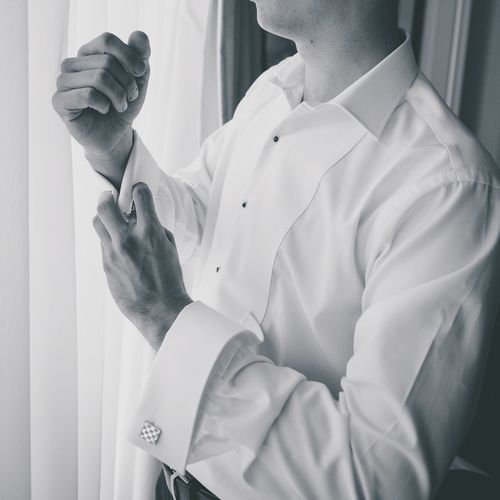 Midsection of man adjusting cuff links by curtain