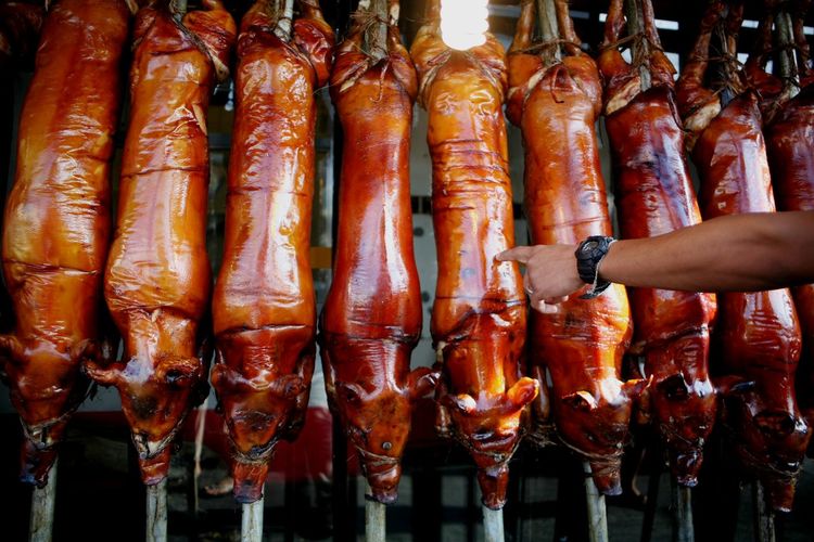Cropped hand pointing at lechon hanging in market for sale