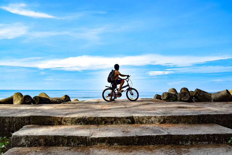 Boy riding bicycle on rocks against sky