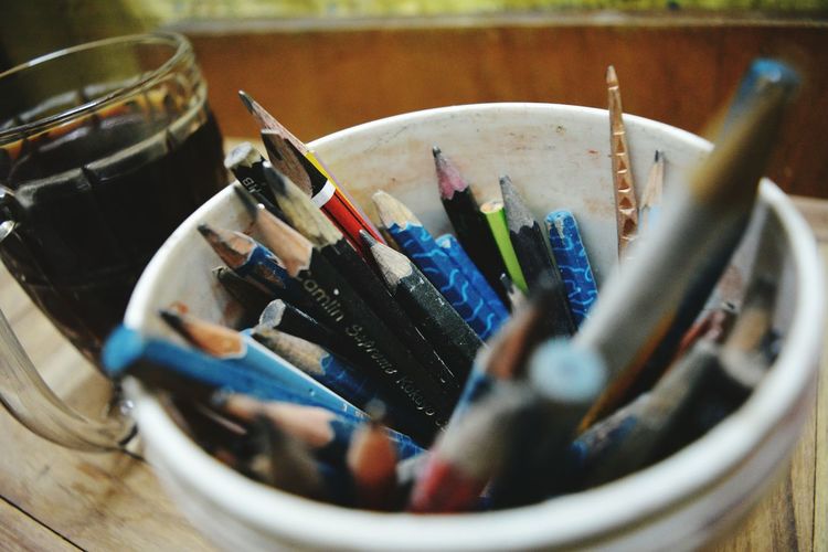 High angle view of pencils and pens in container by drink on table