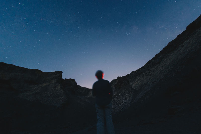 Rear view of man standing on mountain against sky at night