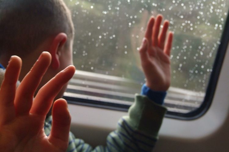 Boy with arms raised looking through window in car during monsoon