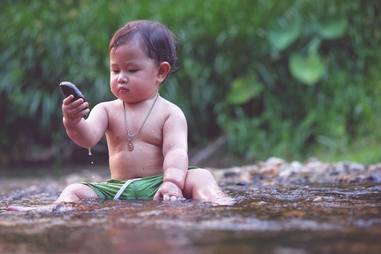 Baby boy holding pebble on stream
