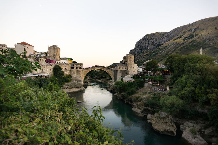Stari most over river neretva in city against clear sky during sunset