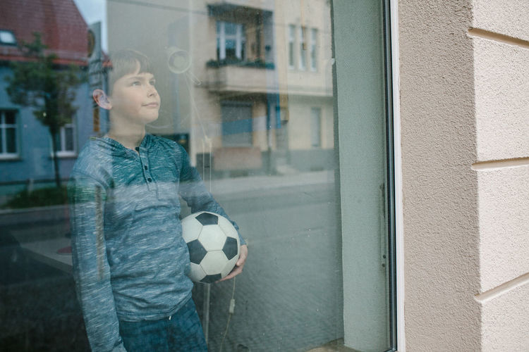 Boy playing with ball in front of window