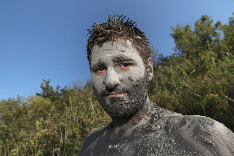 Portrait of man with mud on body against blue sky