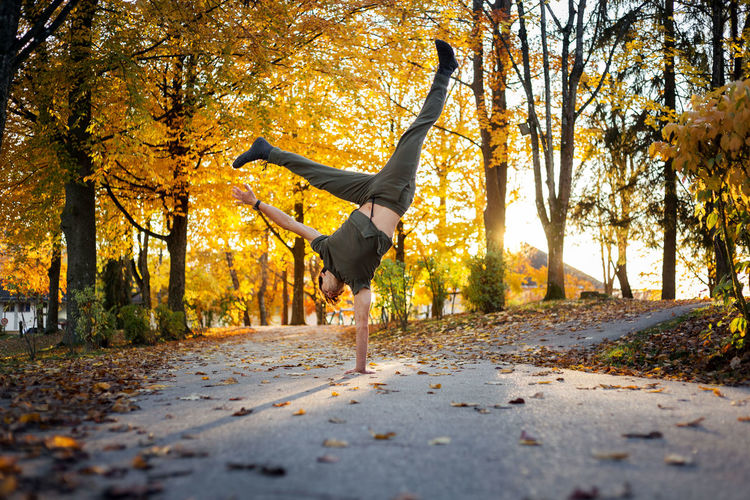 Full length of man doing handstand on road during autumn
