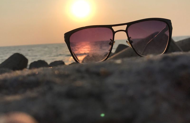 Close-up of sunglasses on beach against sky during sunset