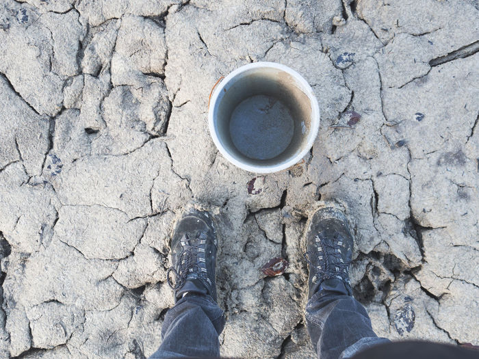 Low section of man standing by empty bucket on cracked landscape