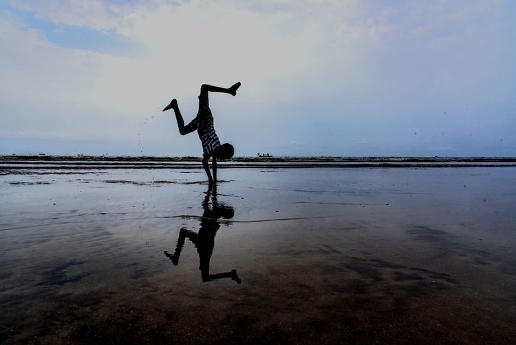 Boy doing handstand with reflection on shore at beach
