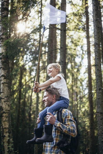 Low angle view of smiling father carrying daughter on shoulder with fishing net in forest