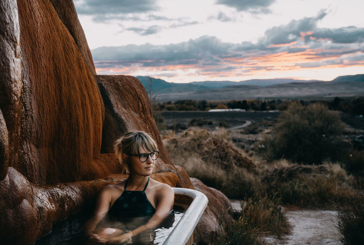 Woman sitting in bathtub at mystic hot springs during sunset