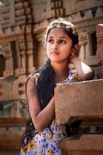 Girl looking away while standing by built structure