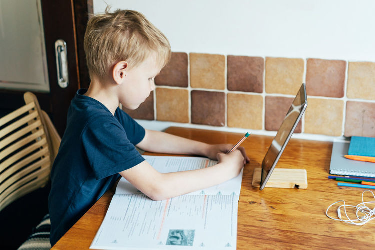 Side view of boy studying on table at home