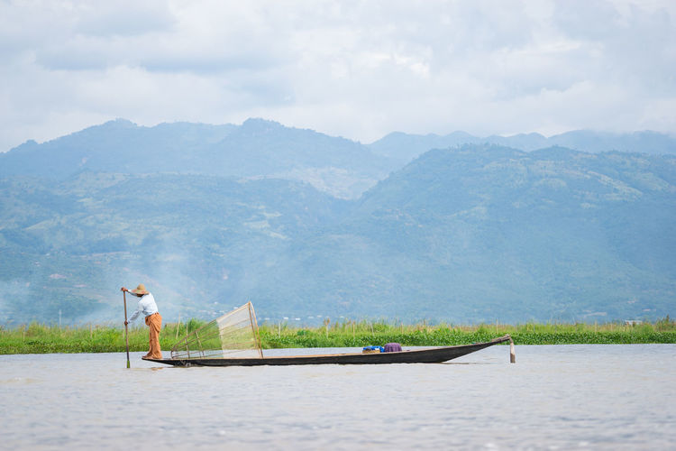 Mid distance of fisherman canoeing on inle lake against mountain