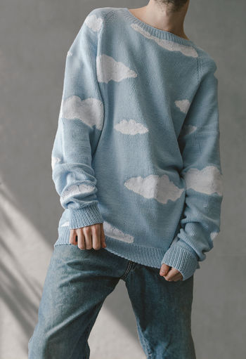 Midsection of man in a sweater with clouds standing against wall