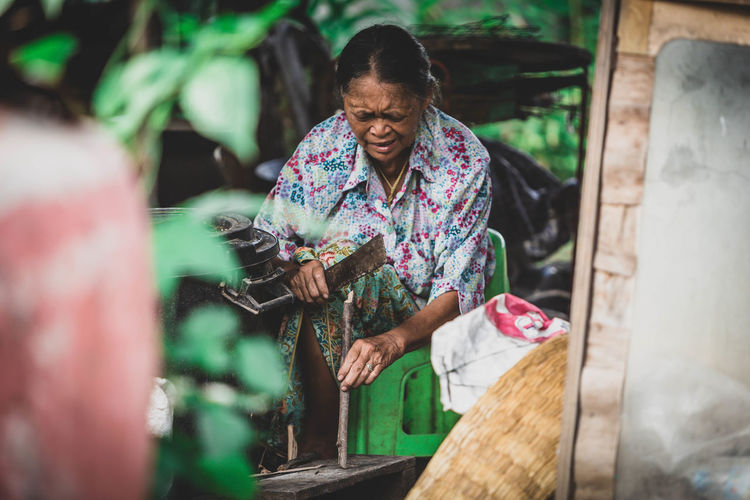 Senior woman cutting stick while sitting outdoors
