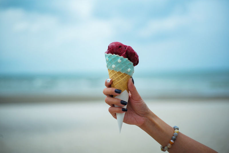 Cropped hand of woman having ice cream cone at beach