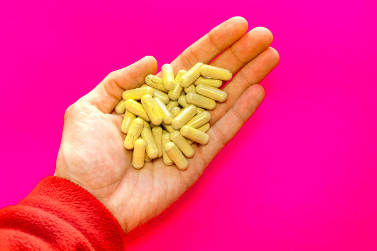 Cropped hand holding pills against yellow background