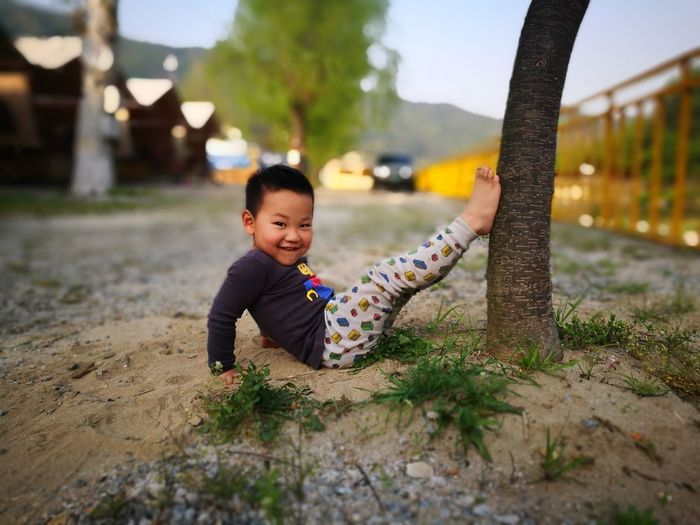 Portrait of cute boy reclining by tree trunk