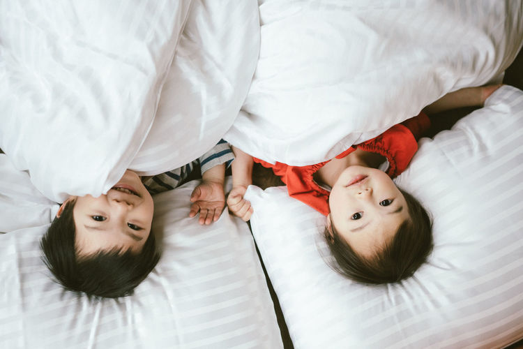 High angle view of siblings lying on bed