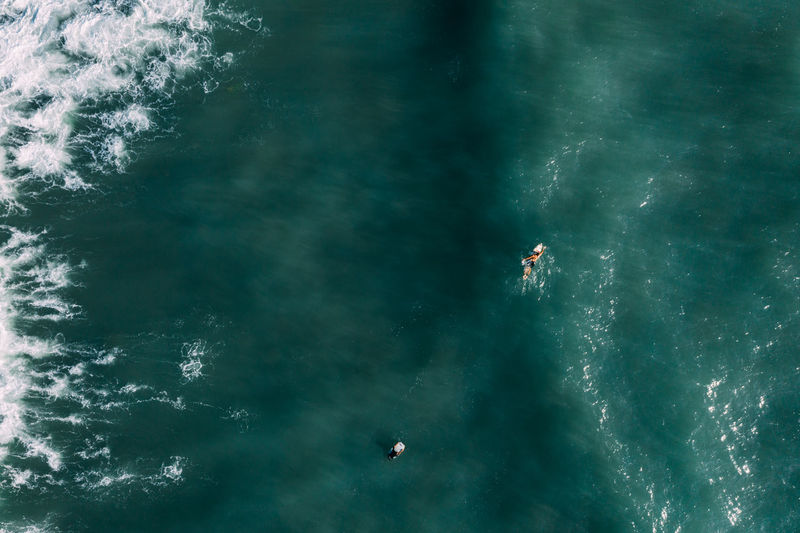 Aerial view of surfers waiting, paddling and enjoying waves in a beautiful blue water