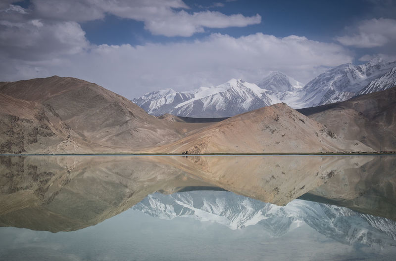 Reflection of mountain on karakul lake against sky