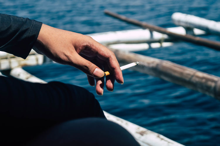 Midsection of person holding cigarette in sea