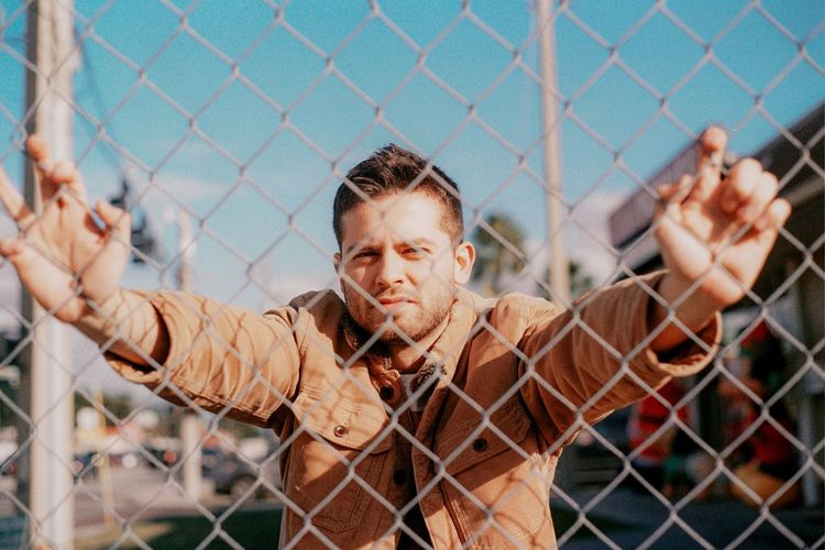 Portrait of man with arms raised against fence