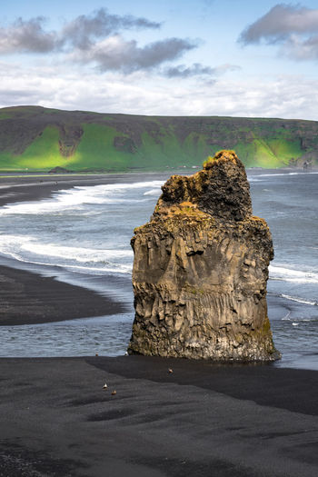 Black snad beach in vik, iceland. big solitaire rock with ocean in background.