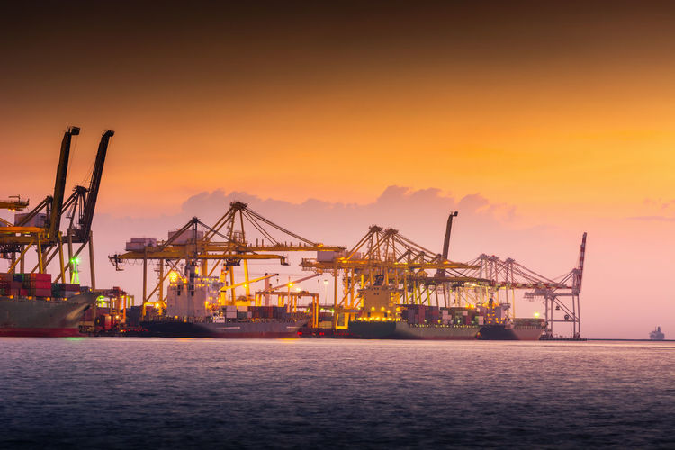 Cranes at commercial dock against orange sky