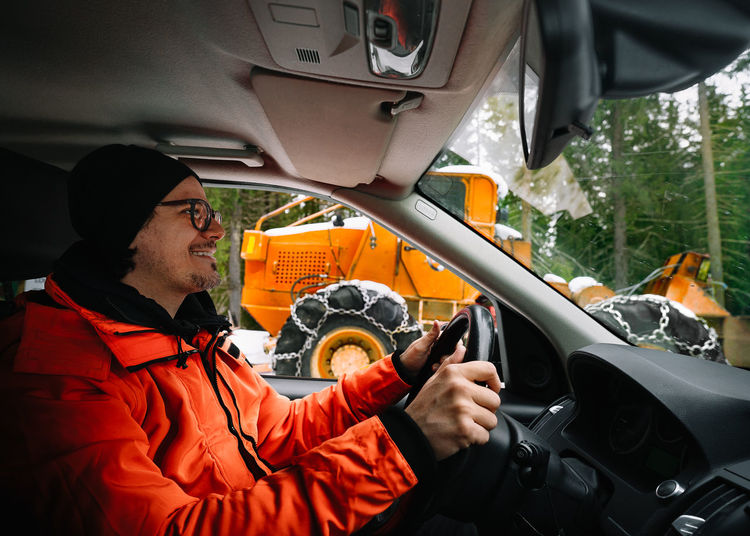 Smiling man in orange jacket driving car on mountain road in winter. car interior. 