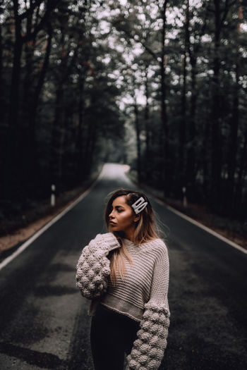Thoughtful young woman standing on road in forest