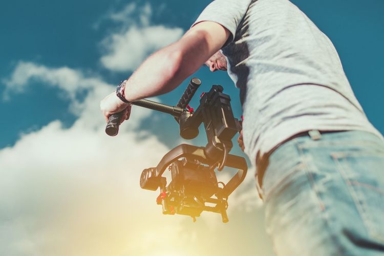 Low angle view of man with television camera against sky