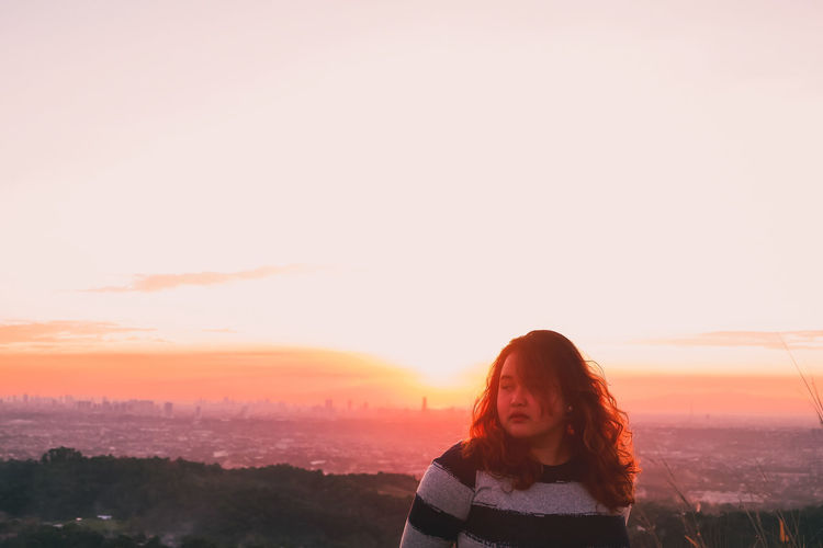 Beautiful young woman standing in city against sky during sunset